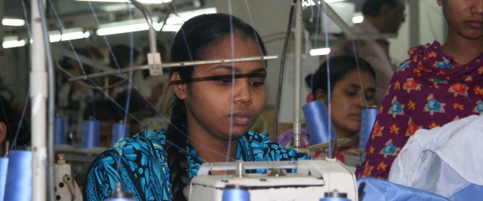 Garment workers sewing at industrial machines in a busy textile factory.