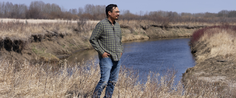 Indigenous person standing in front of a body of water looking off 