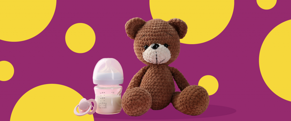 Teddy bear and baby bottle of milk in front of a purple background with yellow polka dots.
