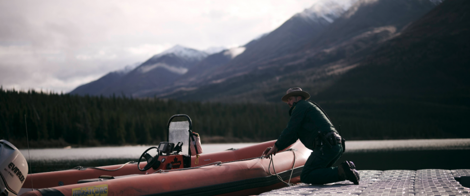 A Parks Canada employee works on a boat outdoors in the Yukon with mountains in the background.