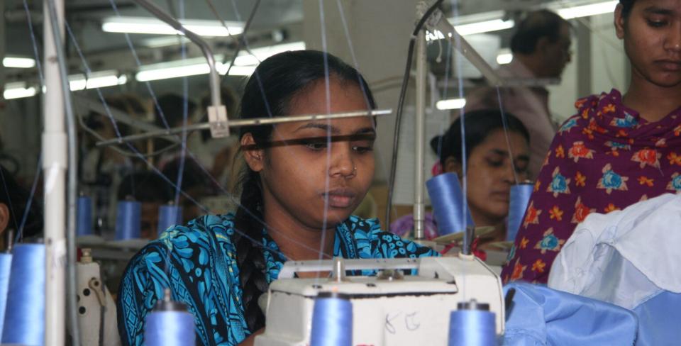 Garment workers sewing at industrial machines in a busy textile factory.