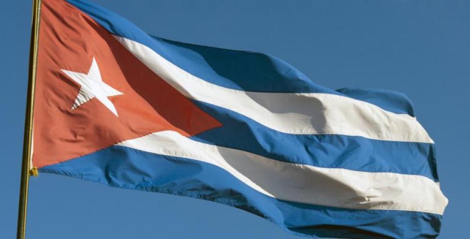 A flag with red, white, and blue stripes waves against a clear blue sky.