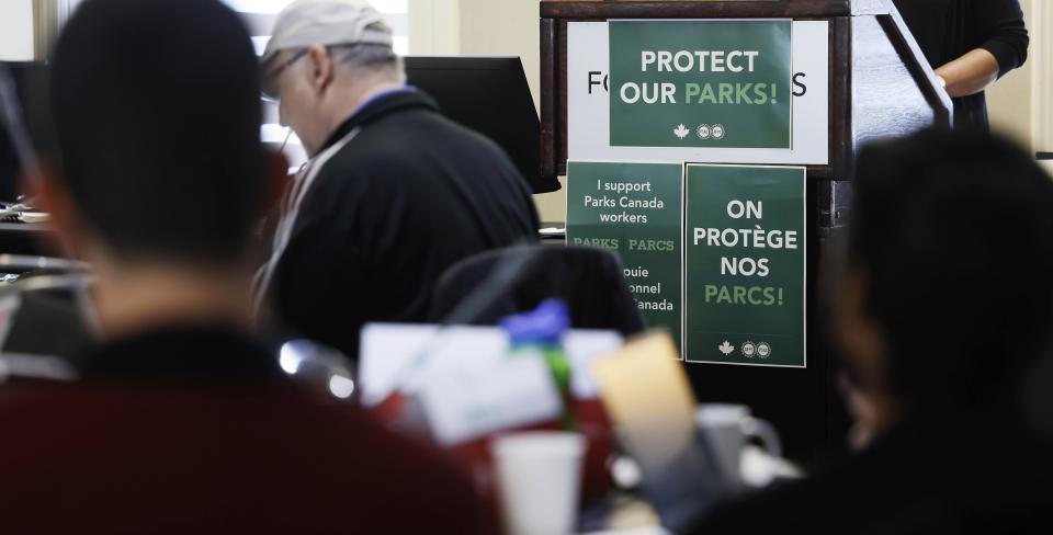 Parks Canada conference photo Participants attend a meeting in support of Parks Canada workers, with signs reading “Protect Our Parks” and “On protège nos parcs” displayed at the podium.