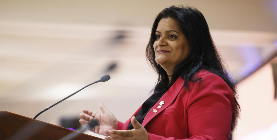 Sharon DeSousa smiling and speaking at a microphone. 