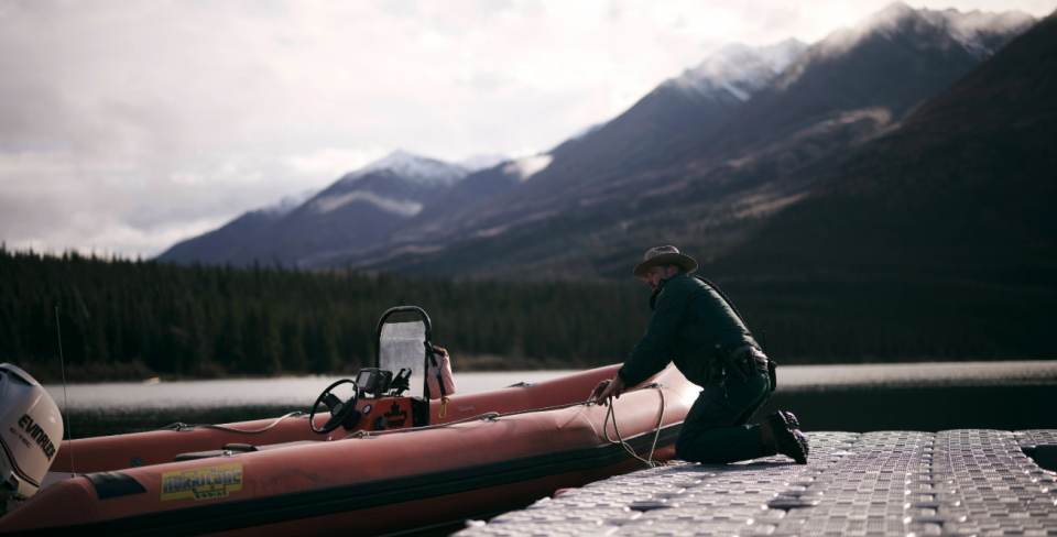 A Parks Canada employee works on a boat outdoors in the Yukon with mountains in the background.